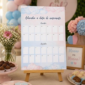 K&ouml;nnte beinhalten: Ein pastellfarbener Kalender auf einer Holzstaffelei, entworfen f&uuml;r eine Babyparty. Der Kalender zeigt blaue und rosa Aquarellwolken und den Text "Adivinha a data de nascimento". Partydekorationen umgeben den Kalender.