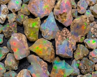 May include: A collection of raw, unpolished opal stones featuring a milky white base with vibrant flashes of neon green, orange, and blue color play. Each stone displays irregular, jagged edges and natural, rough textures throughout the group.