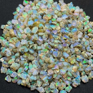 May include: A collection of small, raw opal gemstones featuring a translucent, milky white base with vibrant flashes of iridescent green, blue, and yellow light reflecting from the irregular, multifaceted surfaces of each stone.