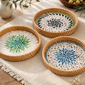 May include: Three round woven rattan trays featuring decorative mosaic tile inlays. One tray displays a green floral pattern, another a blue floral pattern, and the third a black and white spiral design, all set within natural light brown rims.
