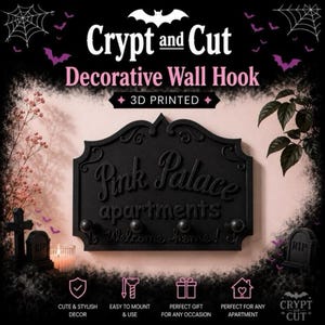 Może przedstawiać: Czarny, dekoracyjny wieszak ścienny z napisem "Pink Palace apartments Welcome home!" i trzema haczykami. Znak jest drukowany w 3D i ma motyw Halloween z nietoperzami i nagrobkami.