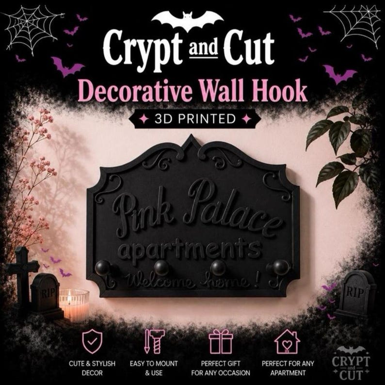 Może przedstawiać: Czarny, dekoracyjny wieszak ścienny z napisem "Pink Palace apartments Welcome home!" i trzema haczykami. Znak jest drukowany w 3D i ma motyw Halloween z nietoperzami i nagrobkami.