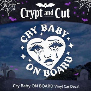 May include: White vinyl car decal with the text "Cry Baby ON BOARD" in a heart shape, featuring a crying face with long eyelashes and a mustache. The decal also includes the text "Crypt and Cut".