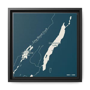 May include: A framed map print featuring a detailed illustration of Greenwood Lake and surrounding areas. The map is in shades of blue and white, with the names of the lake and creek labeled. The print is encased in a black frame.
