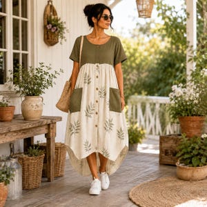 May include: A midi-length dress featuring a solid olive green bodice and a cream-colored skirt with a repeating green leaf pattern. The dress has short sleeves, a button-down front, two large patch pockets, and a high-low hemline.