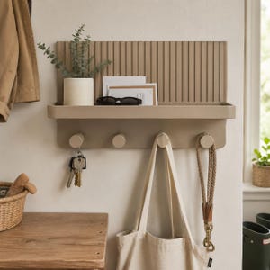 May include: A beige wall-mounted entryway organiser featuring a ribbed back panel, a horizontal shelf, and four cylindrical hooks. The shelf holds a small potted plant, white envelopes, and black sunglasses. A set of keys and a tote bag hang below.