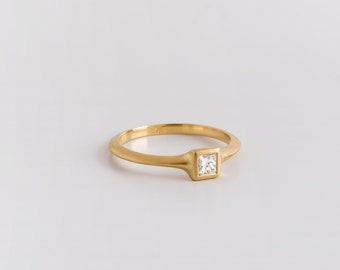 May include: A gold band ring with a square-shaped diamond set in a gold frame.