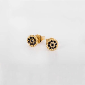 May include: A pair of gold stud earrings with a circular design featuring black gemstones.