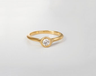 May include: A simple gold band ring with a single round diamond set in a bezel setting.