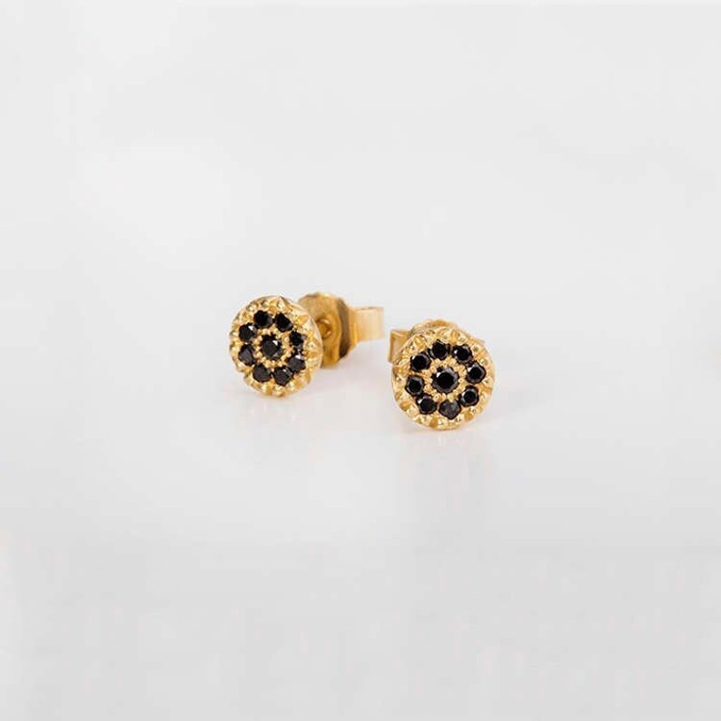 May include: A pair of gold stud earrings with a circular design featuring black gemstones.