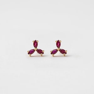 May include: A pair of gold earrings with three ruby-red marquise-shaped stones set in a triangular pattern.