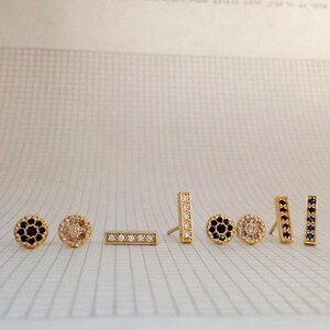 May include: A set of seven gold earrings with different designs. The earrings feature small, round stones in black, white, and pink.