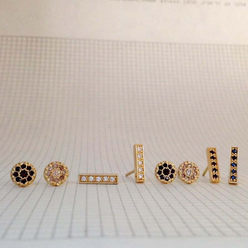 May include: A set of seven gold earrings with different designs. The earrings feature small, round stones in black, white, and pink.