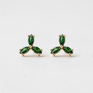 Op de afbeelding: Een paar gouden oorbellen, elk met drie groene, marquisevormige edelstenen.