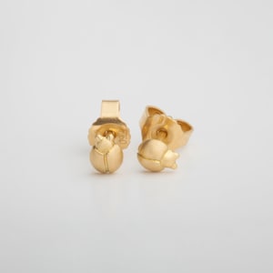 May include: A pair of gold-toned stud earrings featuring a small, detailed beetle design.