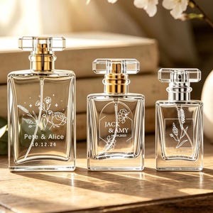 May include: Three clear glass perfume bottles of varying sizes with gold-toned spray nozzles and rectangular caps. Each bottle features white etched floral designs and personalized text, including names like Pete & Alice and Jack & Amy.