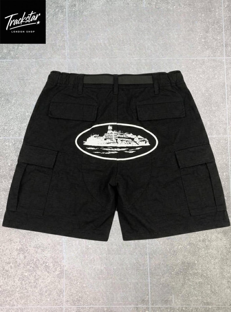 May include: Black cargo shorts featuring an elastic waistband with an integrated black belt. The back displays a white oval graphic containing an illustration of a large ship on water. The shorts include two back pockets and two side cargo pockets.