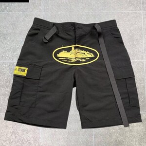 May include: Black cargo shorts featuring a yellow oval graphic of a ship on the front. The shorts include a long black adjustable belt at the waist, two side cargo pockets, and a yellow rectangular patch on the right pocket with the text LITEWORK.