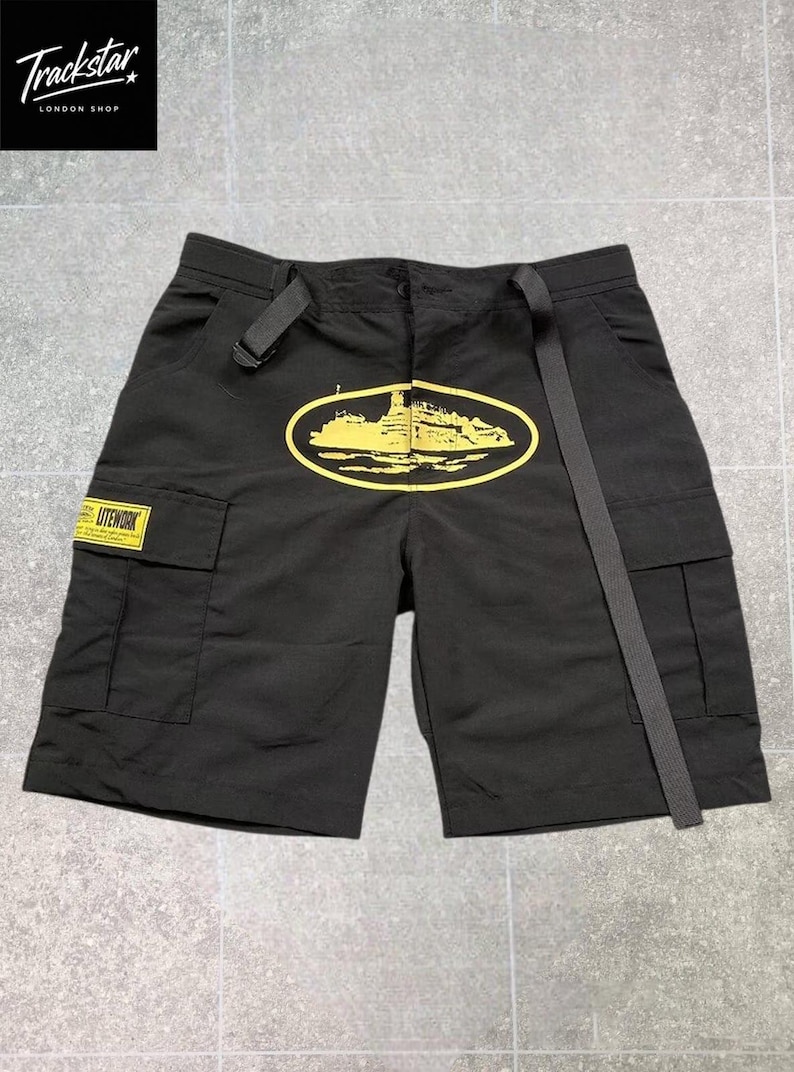 May include: Black cargo shorts featuring a yellow oval graphic of a ship on the front. The shorts include a long black adjustable belt at the waist, two side cargo pockets, and a yellow rectangular patch on the right pocket with the text LITEWORK.