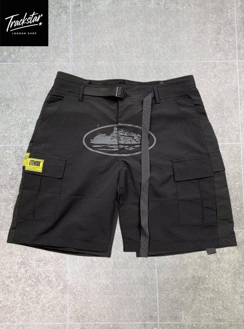 May include: Black cargo shorts featuring an integrated adjustable belt with a buckle, two side cargo pockets, and a yellow rectangular patch with the text LITEWORK. An oval graphic print of a ship is centered on the front of the shorts.