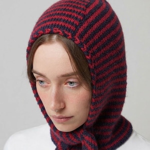 May include: A knitted balaclava featuring horizontal stripes in dark red and navy blue. The headpiece covers the head and neck, with a fitted opening around the face and two long, integrated knitted ties that hang down from the chin area.