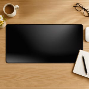 Könnte beinhalten: Eine schwarze rechteckige Schreibtischunterlage auf einer hellen Holzoberfläche. Eine weiße Kaffeetasse, eine kleine Blumenvase, eine Brille, eine Computermaus, ein Notizblock und ein Stift befinden sich ebenfalls auf dem Schreibtisch.