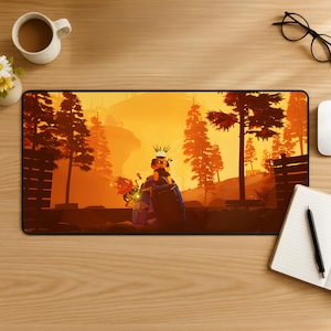 Könnte beinhalten: Eine rechteckige Schreibtischunterlage mit einer leuchtend orangefarbenen und gelben Sonnenuntergangslandschaft, silhouettierten Kiefern und einer zentralen Figur auf einem blauen Fahrzeug. Die Szene enthält ein leuchtendes Element und dunkle Zäune.