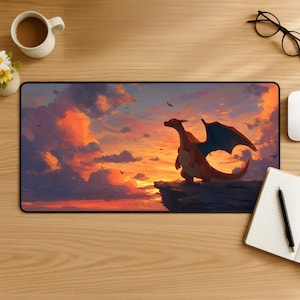 Könnte beinhalten: Eine rechteckige Schreibtischunterlage mit einer lebendigen digitalen Illustration eines zweibeinigen orangefarbenen Drachen mit blauen Flügeln, der auf einer felsigen Klippe steht. Der Hintergrund zeigt einen dramatischen Sonnenuntergang mit orangefarbenen, rosa und violetten Wolken.