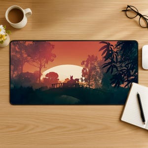 May include: A rectangular desk mat featuring a printed landscape illustration of a silhouette of a person riding a horse across a bridge at sunset. The scene includes dark trees, a large pale sun, and a gradient sky transitioning from orange to red.