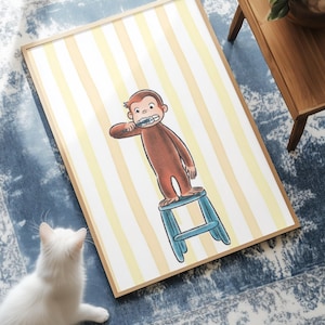 Puede incluir: Una lámina de arte enmarcada que muestra a un mono marrón de pie sobre un taburete azul mientras se cepilla los dientes. El fondo consiste en rayas verticales de color amarillo pálido y blanco. La ilustración está centrada en un marco de madera clara.