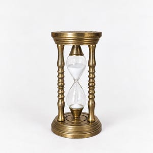Può includere: Una clessidra con una cornice in ottone metallico dalla finitura usurata, composta da una base e una parte superiore circolari collegate da quattro pilastri torniti. Il bulbo centrale in vetro contiene sabbia bianca che scorre verso il basso.