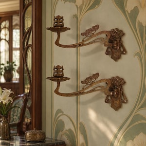 Pode incluir: Dois candeeiros de parede em metal de tom bronze com design de braço articulado. Cada candeeiro possui uma placa decorativa, um braço curvo com detalhes florais e um suporte de vela circular com uma estrutura superior em grade.