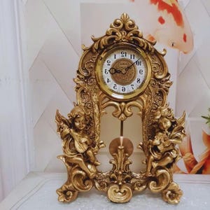 May include: An ornate gold-coloured mantel clock with a round clock face and Roman numerals. The clock features decorative cherub figures and a pendulum. A vintage-style decorative item.