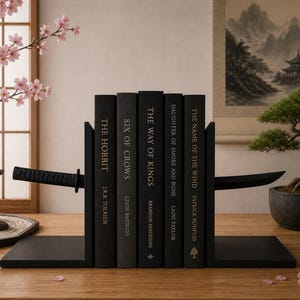 Peut inclure: Un ensemble de serre-livres en métal noir avec un design de sabre katana qui semble traverser une rangée de cinq livres noirs intitulés The Hobbit, Six of Crows, The Way of Kings, Daughter of Smoke and Bone et The Name of the Wind.
