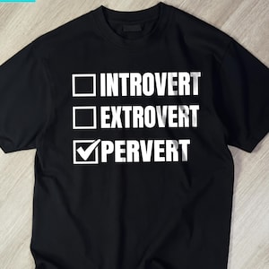 Könnte beinhalten: Ein schwarzes T-Shirt mit kurzen Ärmeln, weißem Text und Kontrollkästchen. Die Grafik zeigt drei Optionen: ein leeres Kästchen neben INTROVERT, ein leeres Kästchen neben EXTROVERT und ein angekreuztes Kästchen neben PERVERT in fetter Schrift.