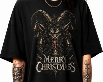 May include: A black short-sleeve t-shirt featuring a graphic of a horned creature with a long tongue, surrounded by hanging bells and holly. The text MERRY CHRISTMASS is printed in a gothic font below the creature. The shirt has a crew neckline.
