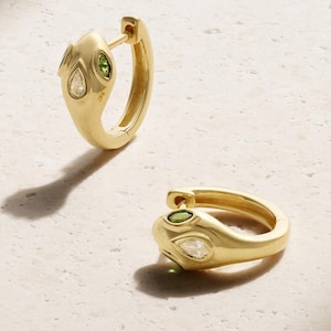 Può includere: Un paio di orecchini a cerchio in oro a forma di serpente. Ogni orecchino presenta una finitura in oro lucido con una piccola pietra chiara a forma di pera e una pietra verde taglio marquise incastonate nella testa del design a serpente.