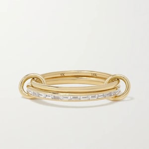 Op de afbeelding: Een 18-karaats geelgouden ring met een centrale band bezet met een rij heldere stenen in baguette-slijpvorm. De centrale band is aan beide zijden verbonden met een effen gouden buitenband door middel van twee ronde gouden schakels. De binnenzijde is gestempeld met SK 18K.