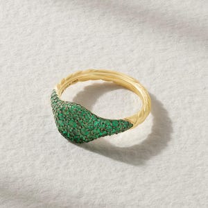 Può includere: Un anello chevalier in oro con una superficie arrotondata densamente incastonata con numerose piccole pietre preziose di colore verde brillante. La fascia presenta una texture intrecciata a corda sul bordo esterno e reca l'incisione 750.