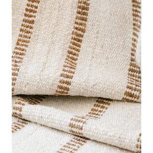 May include: A woven textile featuring a thick, cream-colored base with vertical, textured brown stripes. The fabric has a visible, chunky weave pattern with a soft, slightly raised surface texture, creating a consistent striped design throughout.