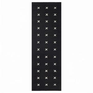 Puede incluir: Una alfombra rectangular de color negro con un patrón repetitivo de pequeños símbolos de cruz en blanco dispuestos en tres columnas verticales. El diseño consta de doce filas de estas marcas blancas espaciadas uniformemente.