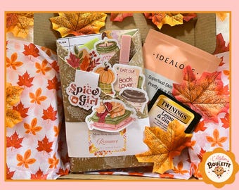 Peut inclure: Un coffret cadeau contenant un livre emballé, un sachet de thé Twinings Lemon & Ginger et un sachet de soin Idealove. L'ensemble est décoré de découpes de feuilles d'automne et d'autocollants représentant une citrouille, un café et un chat.
