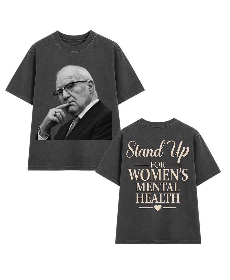 May include: A charcoal grey short-sleeve t-shirt featuring a black and white photographic print of a person in a suit and glasses on the front. The back displays the beige text Stand Up FOR WOMEN'S MENTAL HEALTH with a small heart icon below.