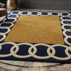 May include: A rectangular area rug featuring a solid mustard yellow centre panel surrounded by a wide navy blue border. The border is decorated with a repeating pattern of interlocking cream-coloured circles that form a continuous chain around the rug.