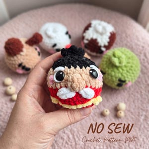 Peut inclure: Un petit jouet en peluche crocheté et rond avec un chignon noir, de grands yeux noirs, un nez beige et une moustache blanche, portant une tenue rouge et jaune. Le texte NO SEW Crochet Pattern PDF est visible en bas à droite.