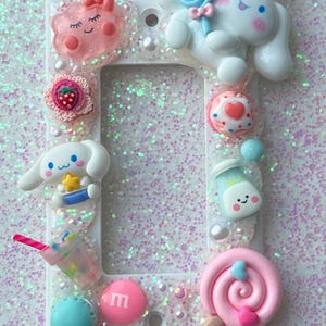 May include: A white light switch cover decorated with pastel pink, blue, and yellow characters, candy, and a milk carton. The background is covered in iridescent glitter.