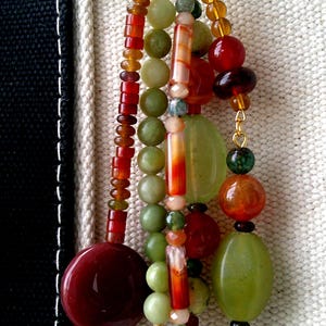 May include: A decorative keychain featuring multiple strands of assorted beads in shades of green, amber, and deep red. The beads vary in shape, including round, cylindrical, and oval forms, all suspended from a gold-toned metal ring clasp.