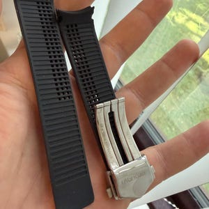 May include: Two black watch straps with a silver clasp. The straps are made of a textured rubber material with a series of rectangular perforations. The clasp is engraved with the brand name "TAGHeuer".