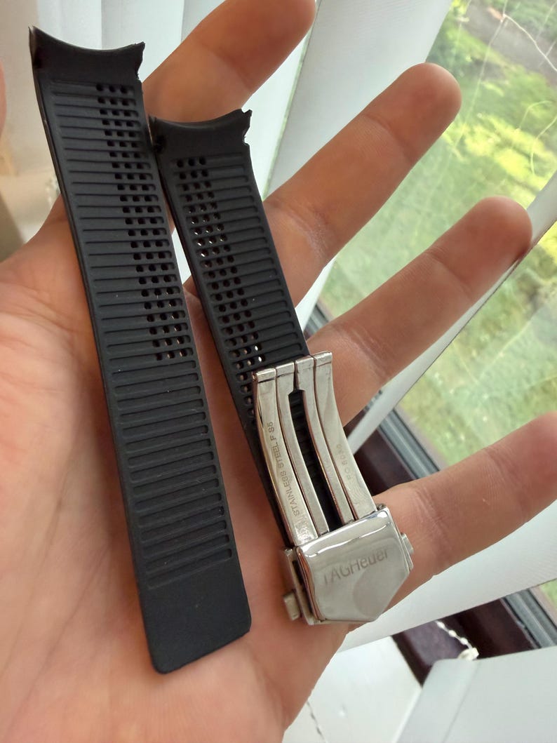 May include: Two black watch straps with a silver clasp. The straps are made of a textured rubber material with a series of rectangular perforations. The clasp is engraved with the brand name "TAGHeuer".