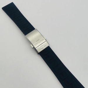 May include: A black rubber watch strap featuring the embossed word BREITLING along the band. The strap includes a brushed silver-tone metal deployment clasp engraved with the text BREITLING 1884 and a small winged logo emblem on the surface.